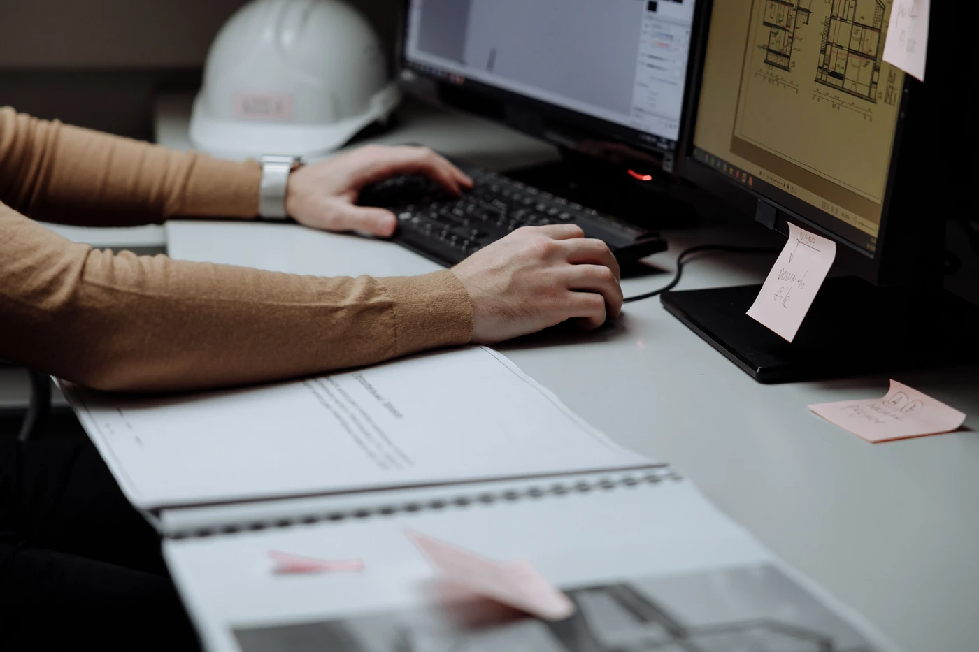 Ingénieur du bureau d’études travaillant sur des plans techniques en CAO, casque de chantier posé sur le bureau.